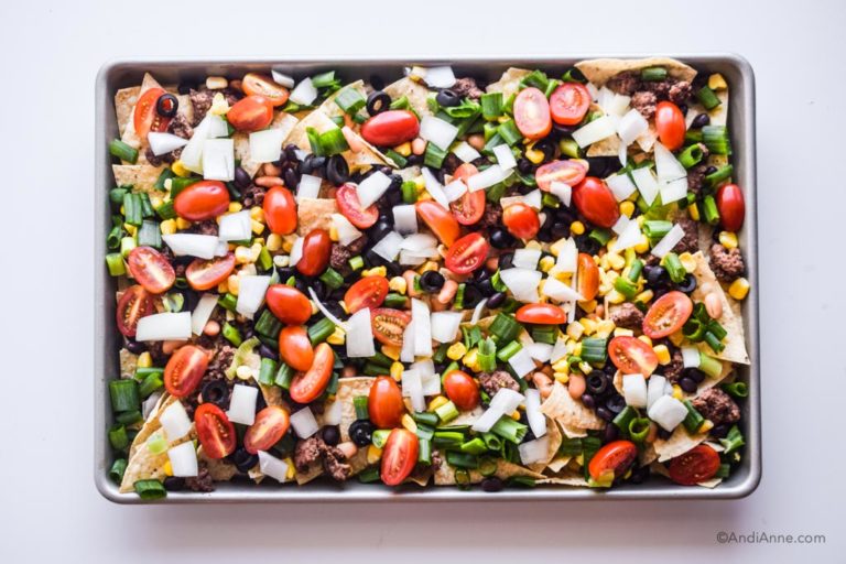 sliced veggie toppings spread evenly over tortilla chips on the sheet pan
