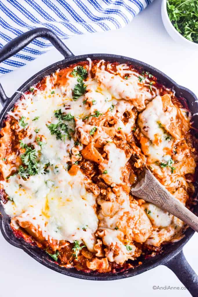 skillet lasagna with wooden spoon and striped napkin and parsley in bowl