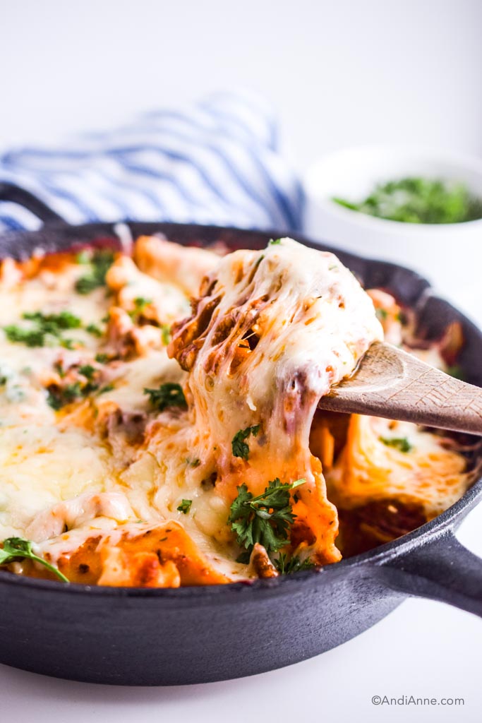 wooden spoon pulling up melted cheese from lasagna in skillet