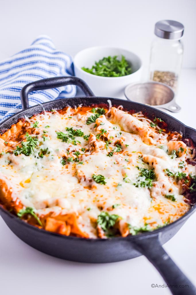 skillet lasagna with white bowl, blue and white striped napkin and steel bowl in background