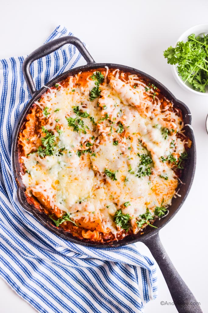 skillet lasagna with striped napkin and small bowl of parsley surrounding it