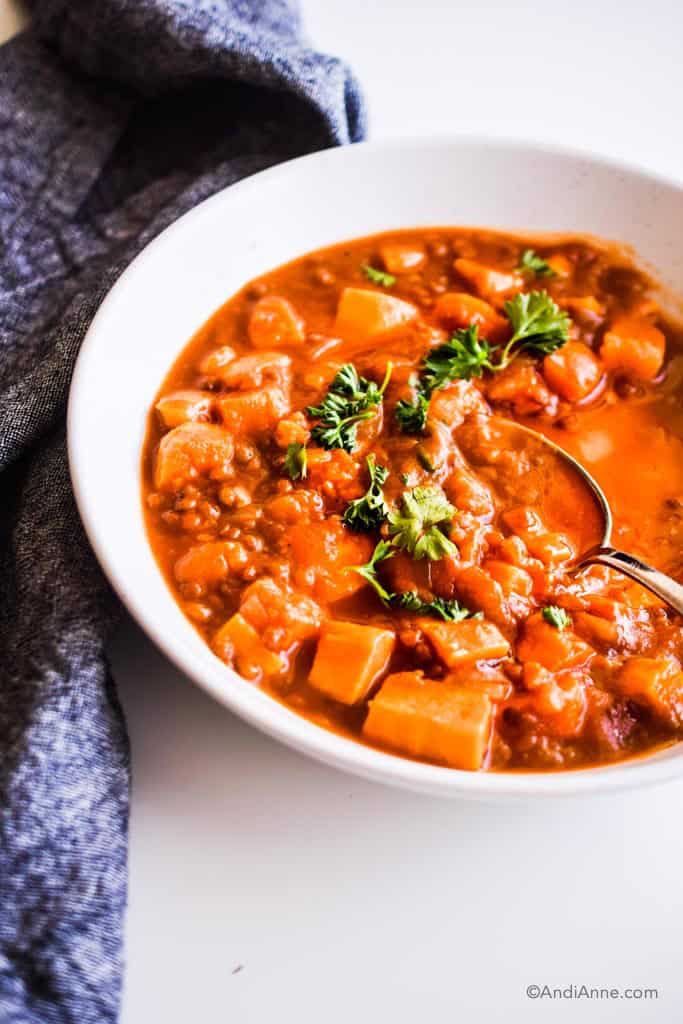 close up detail of sweet potato soup in white bowl with chopped parsley and dark napkin