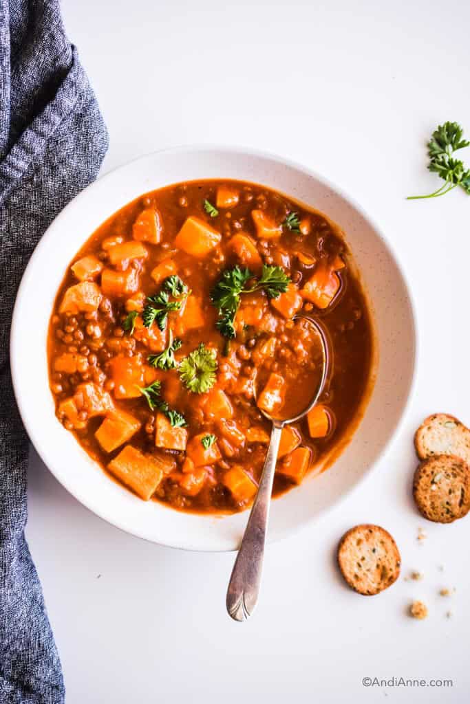 sweet potato lentil pumpkin soup in a white bowl with crackers and a dark napkin surrounding it