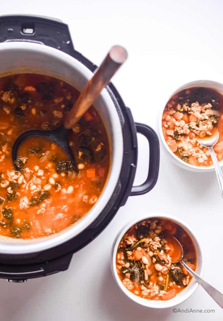Ground turkey soup with kale and beans in a pressure cooker with wooden spoon and two white bowls of soup beside it