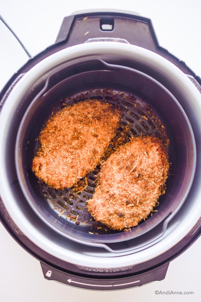 looking into an air fryer with cooked parmesan chicken breasts inside