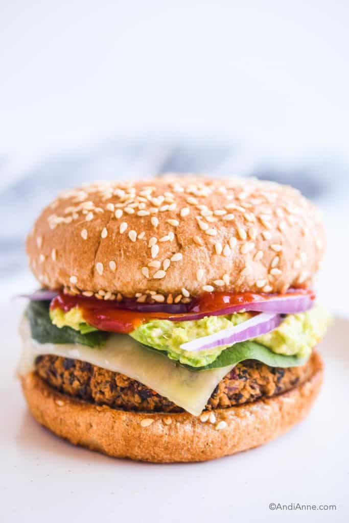 black bean burger on a plate with toppings including melted cheese, spinach, mashed avocado, ketchup, and sliced onion.