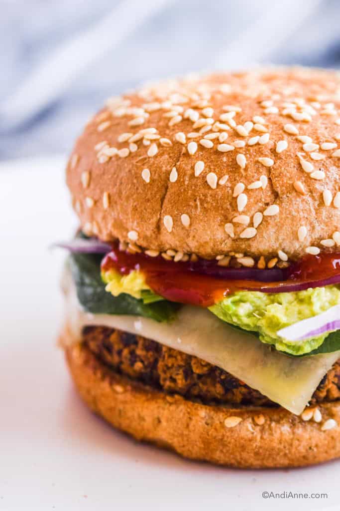 side close up detail of the burger piled high with toppings and a sesame hamburger bun on a white plate