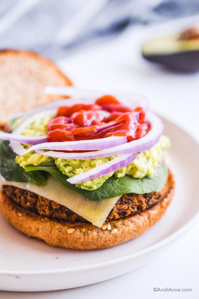 black bean burger without the top bun piled with cheese, spinach, avocado, onion and ketchup