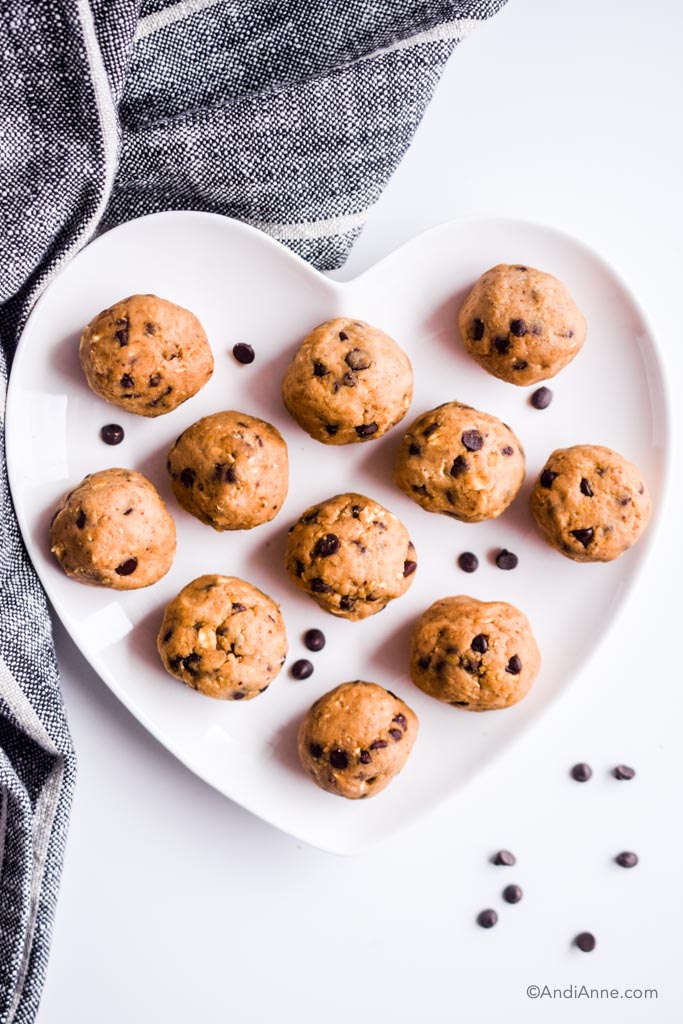 cookie dough energy bites on a white heart shaped plate with a few chocolate chips sprinkled around them.