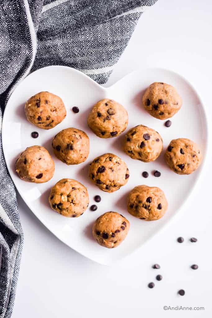cookie dough energy bites on a white heart shaped plate with a few chocolate chips sprinkled around them.
