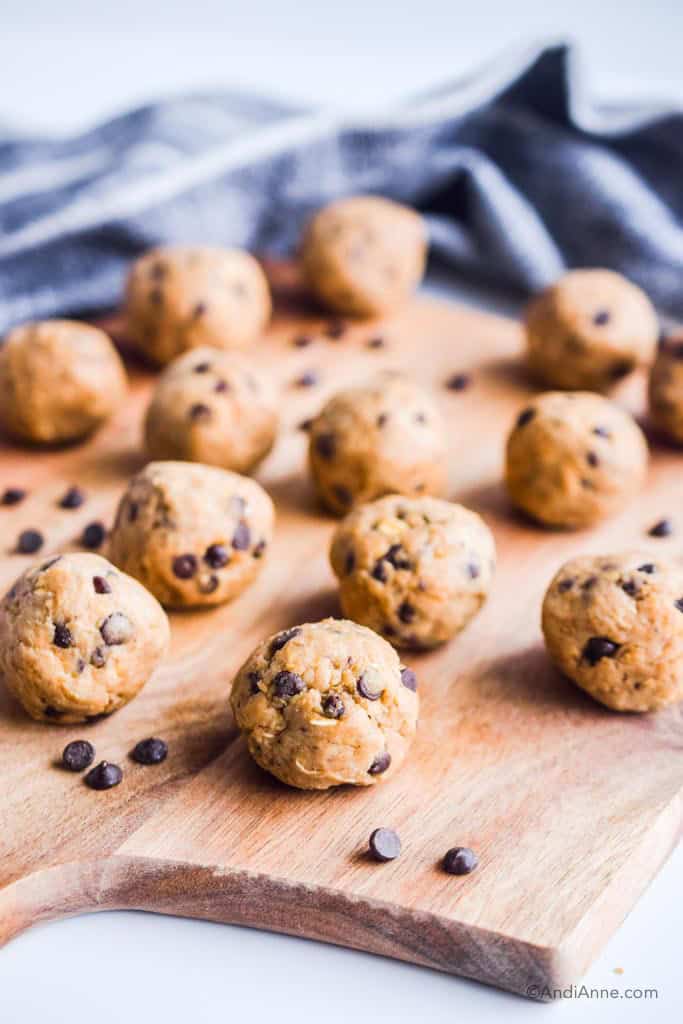 cookie dough energy bites on a cutting board with chocolate chips around them. Dark grey napkin in the background.