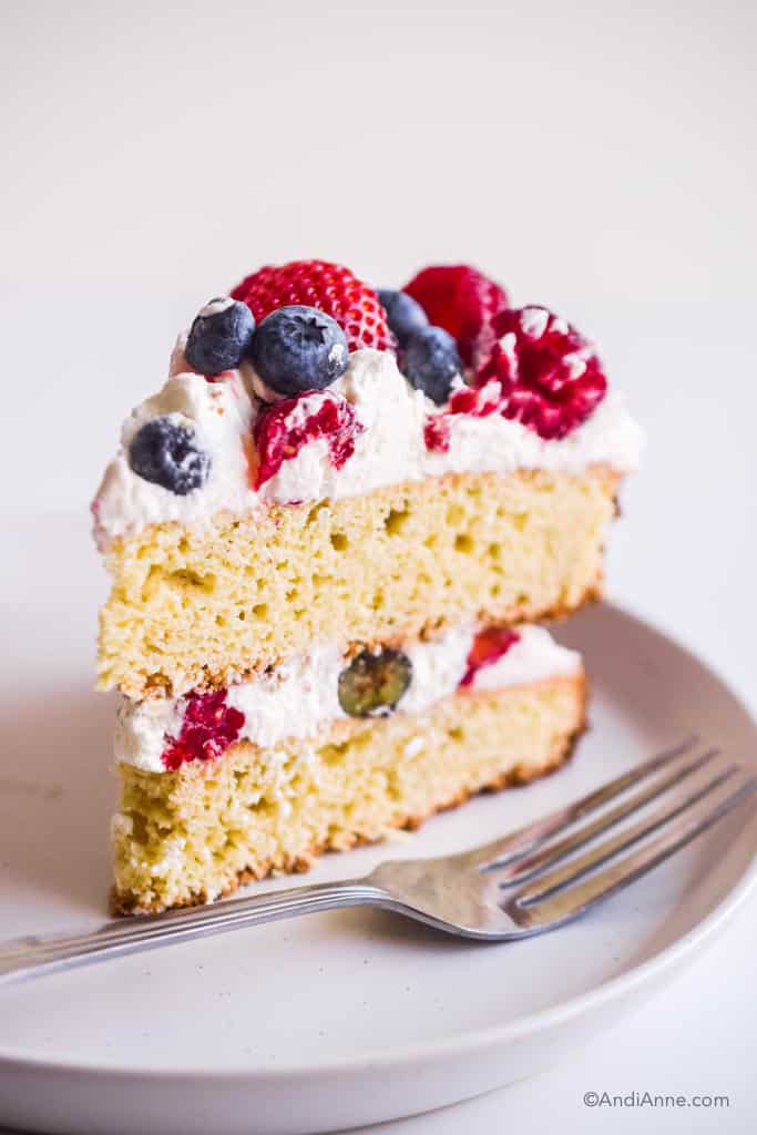 slice of gluten free white cake with whipped cream and berries in the center and on top