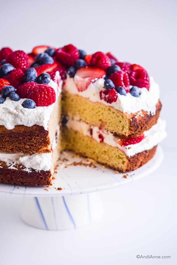 Slice cut out of gluten free cake. Fresh berries on top with whipped cream, on white cake stand.