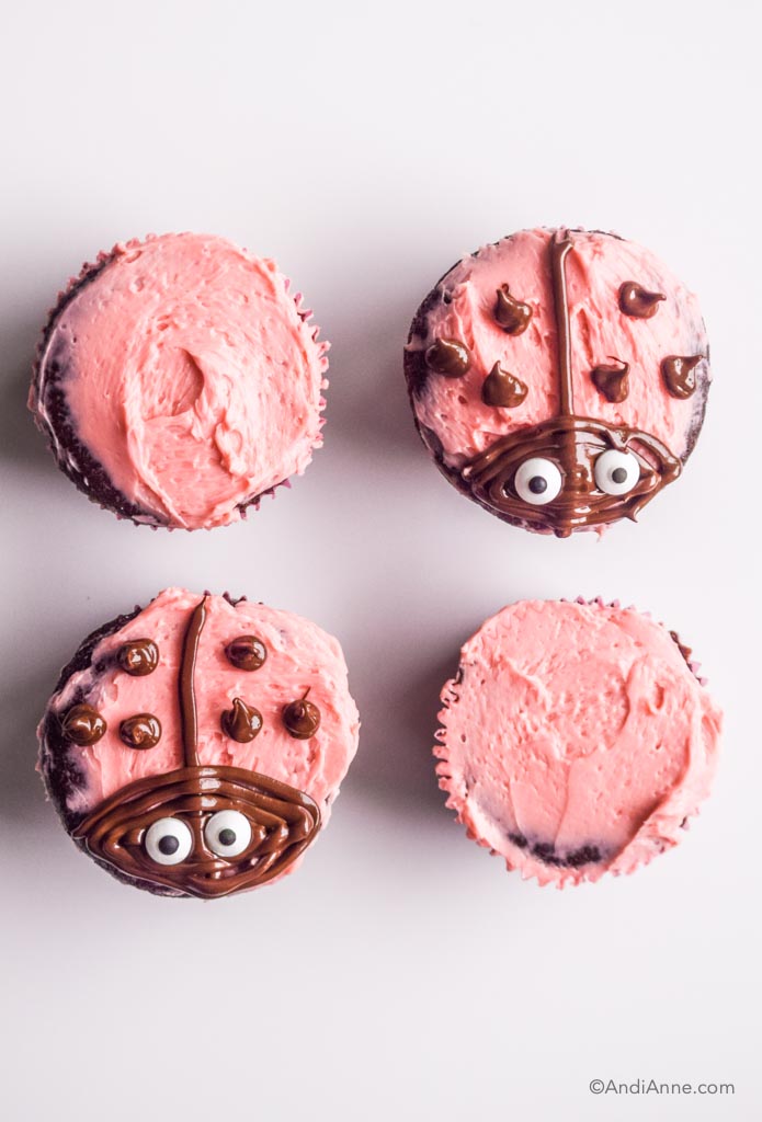 four chocolate cupcakes with pink icing. Two have ladybug decorations on top.