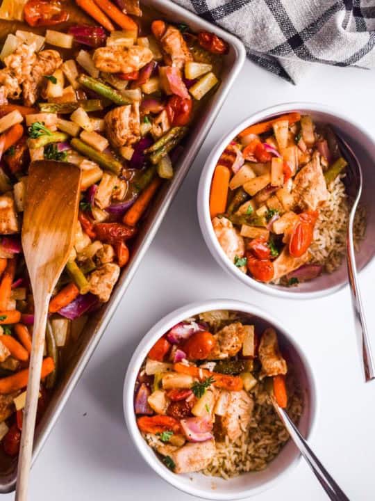 pineapple chicken sheet pan dinner beside two white bowls with rice and roasted veggies and chicken
