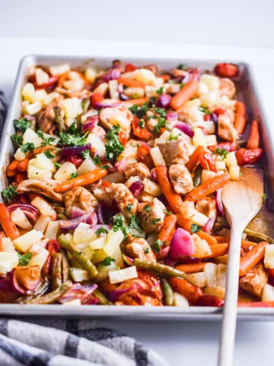 side view of pineapple chicken sheet pan dinner with wood spatula