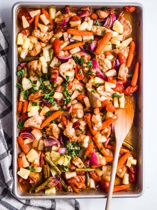 pineapple chicken sheet pan dinner with wood spatula and plaid checkered kitchen towel beside it