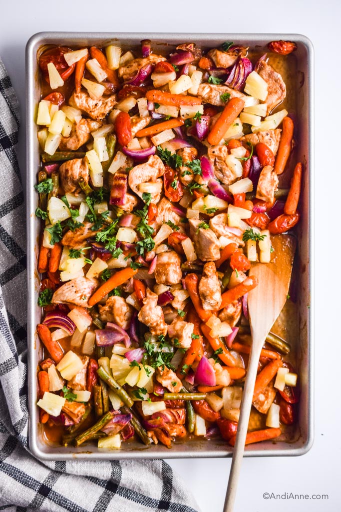 pineapple chicken sheet pan meal with wooden spoon and kitchen towel beside it