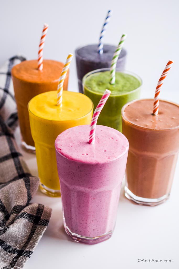 six colorful healthy smoothies in glasses with paper straws. 