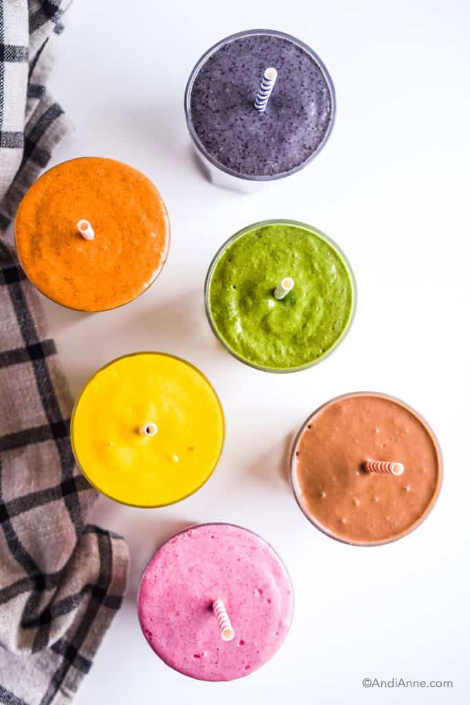 looking down at the tops of six smoothies in glasses with straws from above.