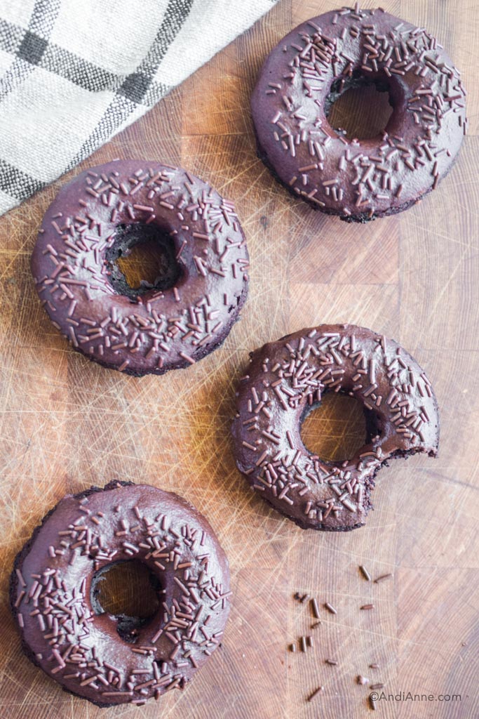 chocolate baked donuts with chocolate glaze and sprinkles on a wood cutting board.