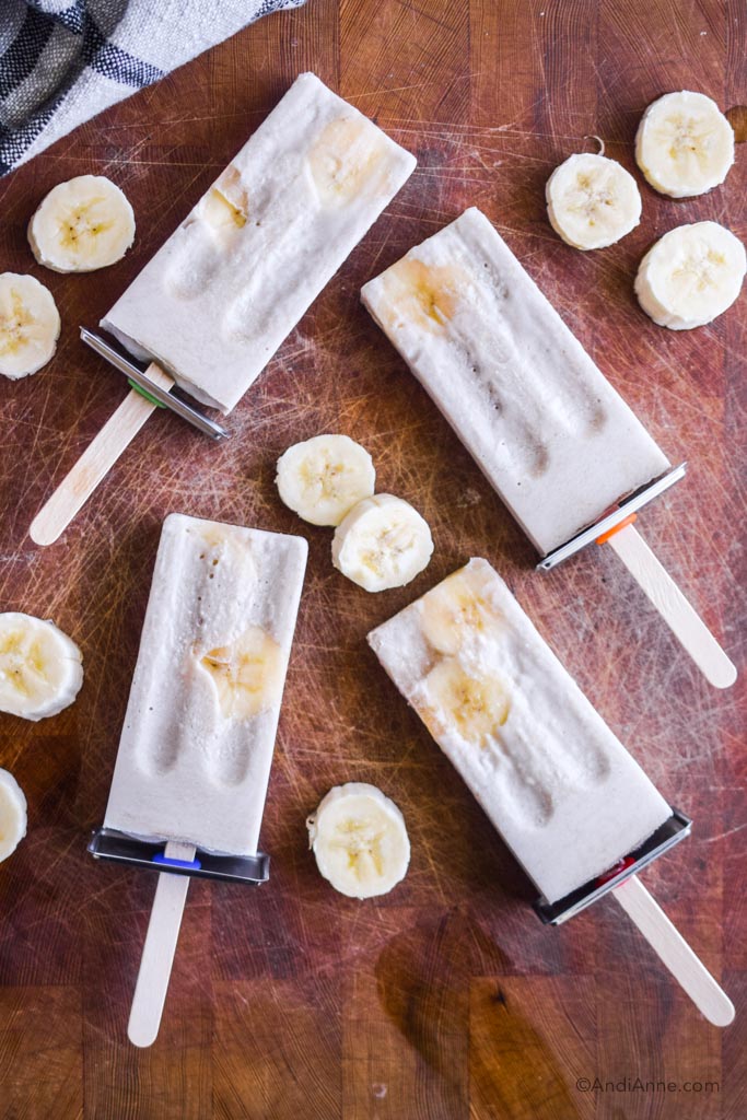 banana cream popsicles on a wood cutting board with banana slices