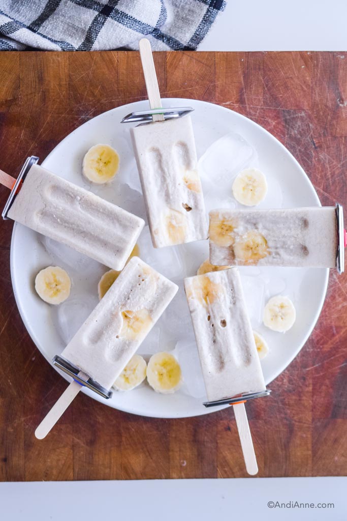 banana cream popsicles on a white plate with ice cubes and banana slices