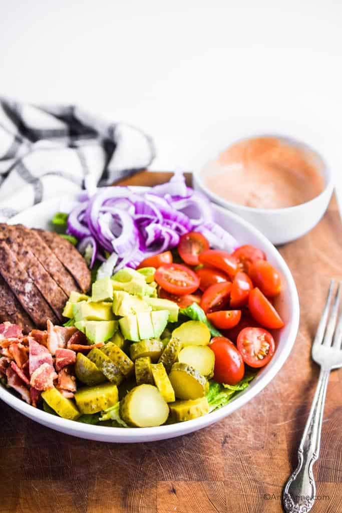 burger salad bowl with special sauce dressing in side bowl. forke and kitchen towel beside them