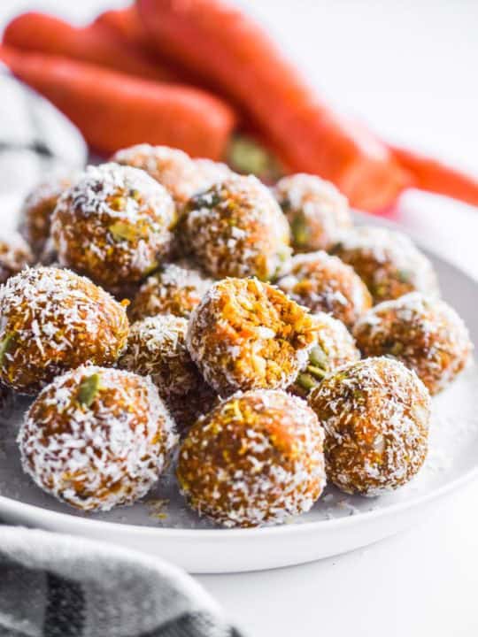 carrot cake bites on a white plate with carrots in the background