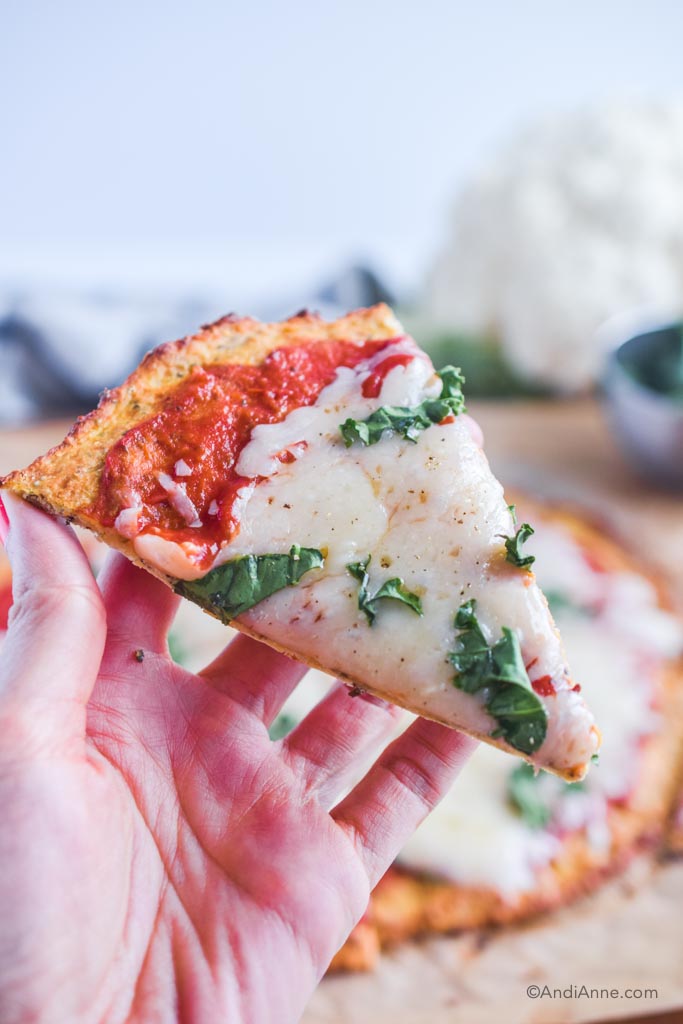 hand holding one slice of margherita pizza with cauliflower crust