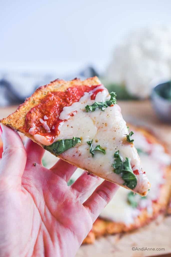 hand holding one slice of margherita pizza with cauliflower crust