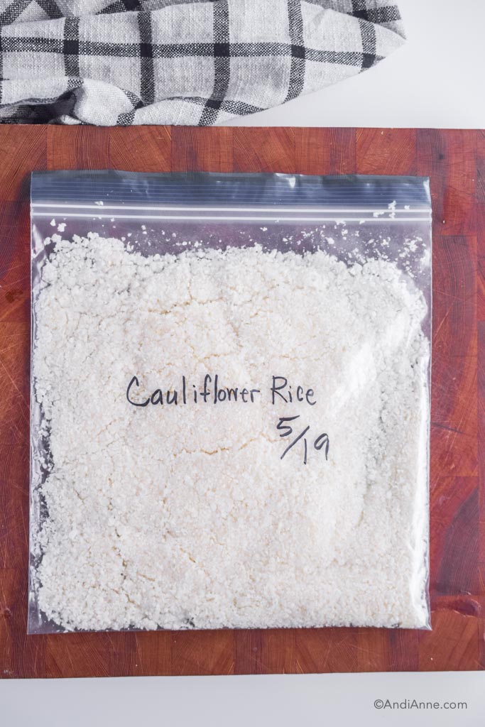 riced cauliflower in a freezer bag laying flat on a cutting board with name and date written on the front