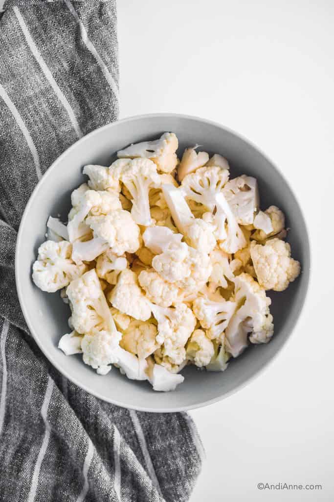 chopped cauliflower in a blue bowl with a striped kitchen towel beside it