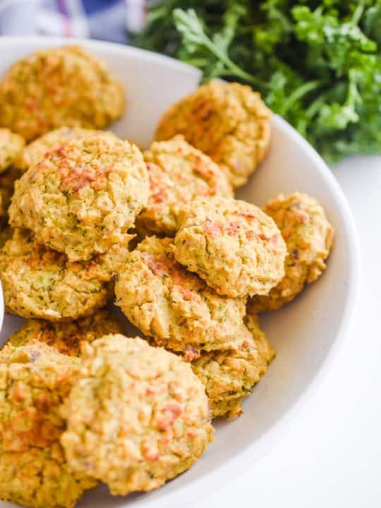 Close up detail of chickpea nuggets on a white plate. Green parsley is in the background.