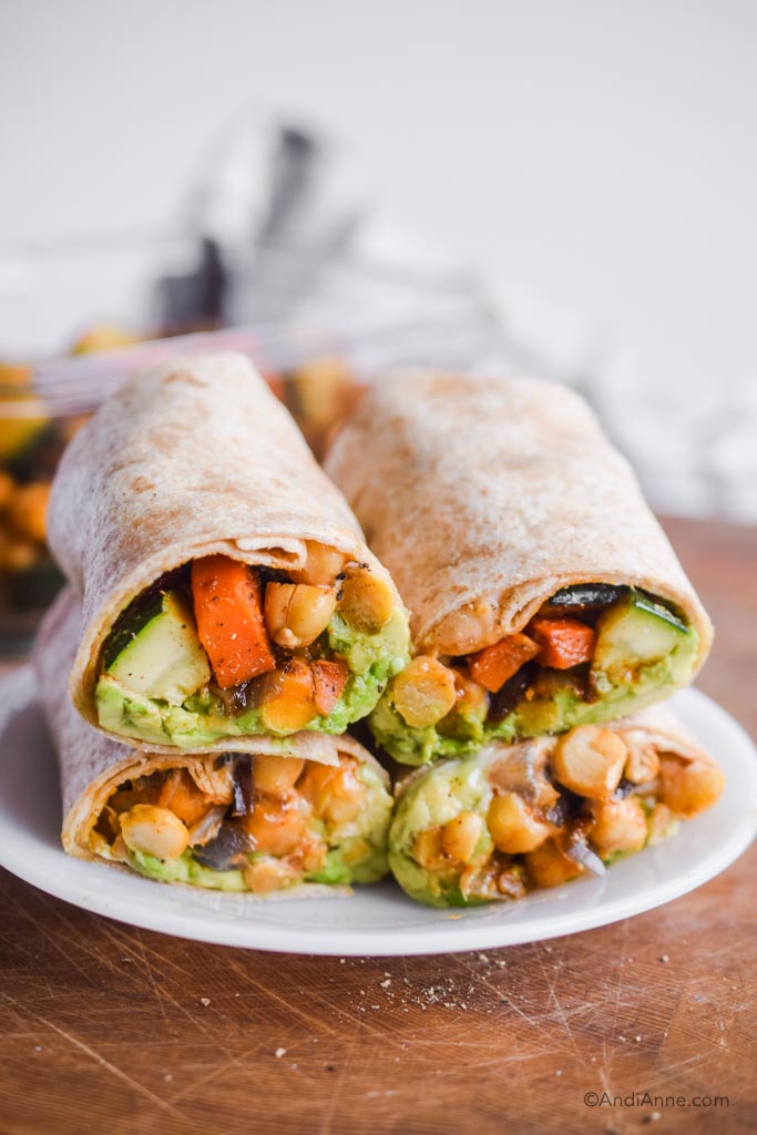 Four wraps with chopped zucchini, carrots, chickpeas and avocado inside. 