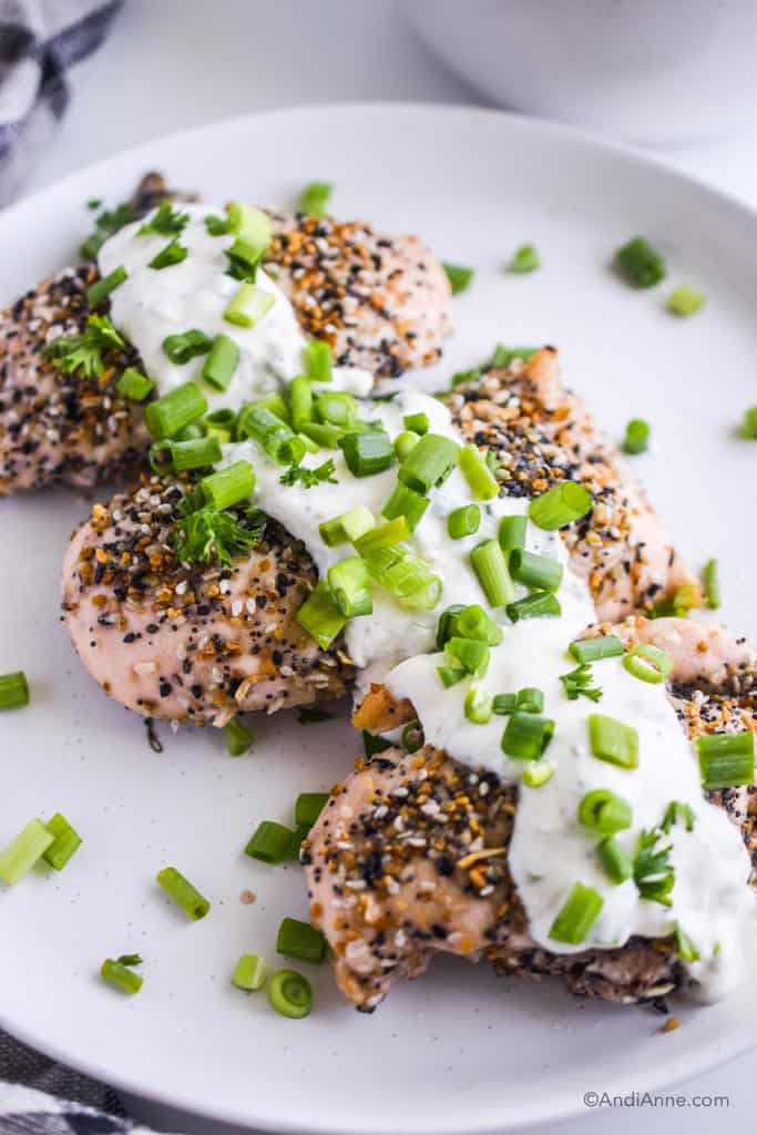 everything bagel chicken breasts on a white plate with greek yogurt dressing and sliced green onions sprinkled on top