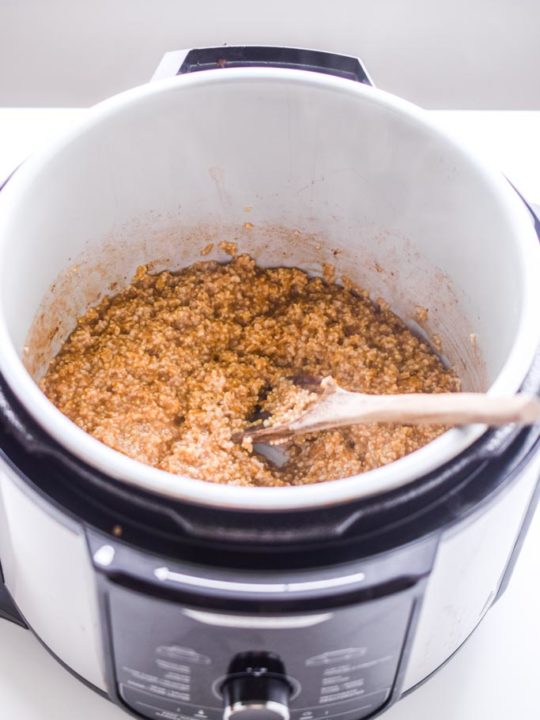 cooked steel cut oats inside an instant pot with a wooden spoon