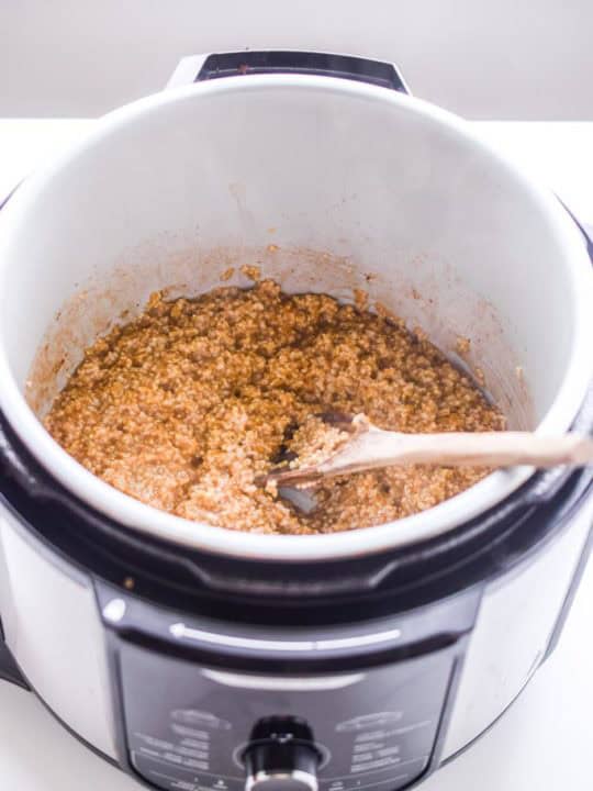 cooked steel cut oats inside an instant pot with a wooden spoon