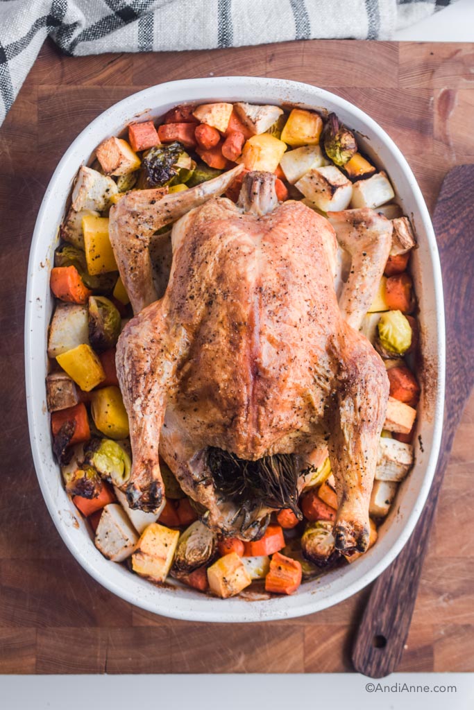 roasted chicken with root vegetables in a white dish with wood cutting board