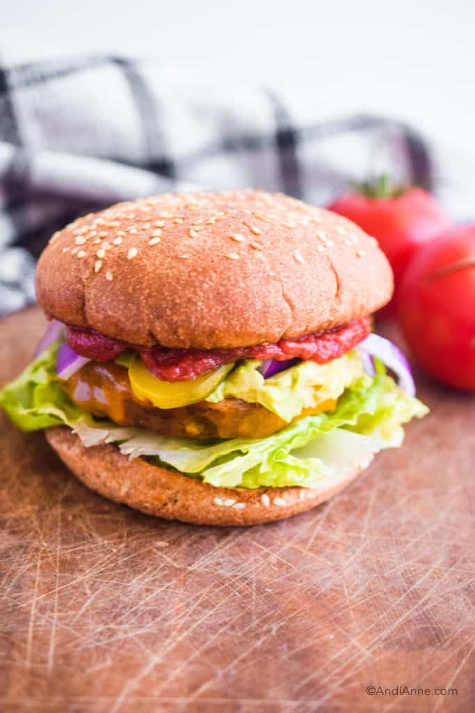 air fryer hamburgers on a bun with lettuce cucumber and ketchup. tomatoes and kitchen towel in background.