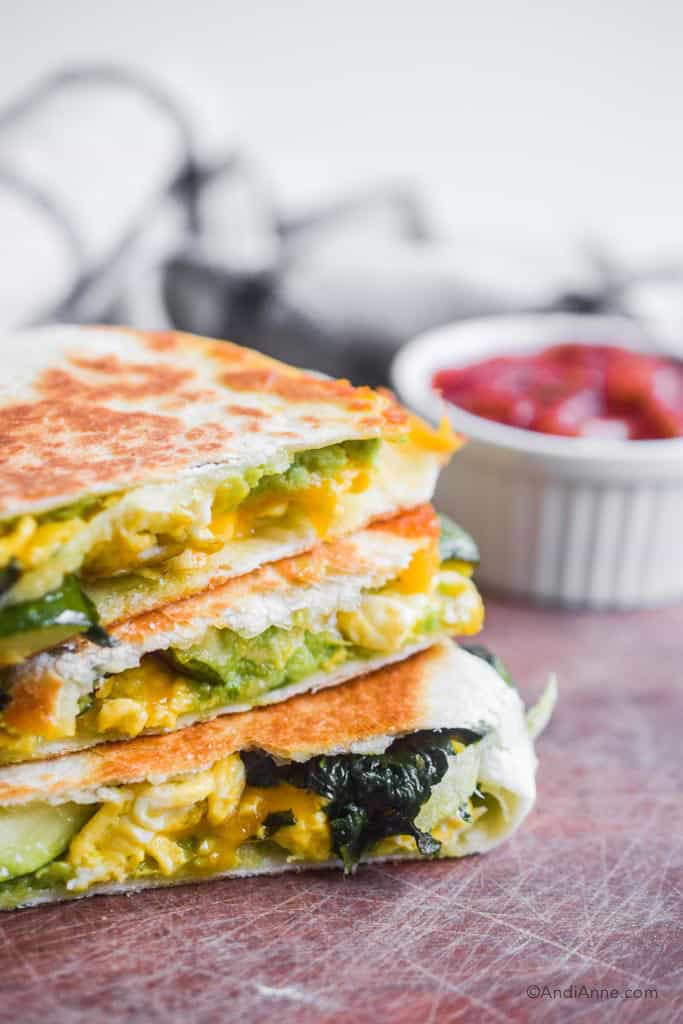 close up detail of zucchini spinach quesadilla with mashed avocado. white bowl if salsa in background.