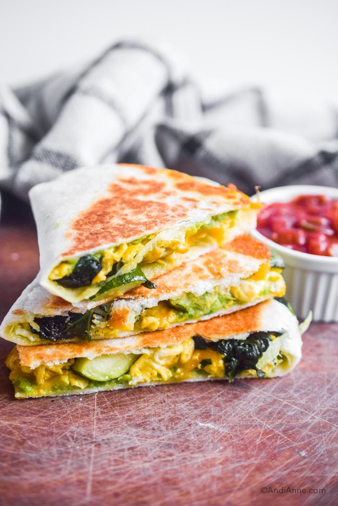 Zucchini, egg, spinach quesadillas stacked on top of each other with a bowl of salsa in the background. 