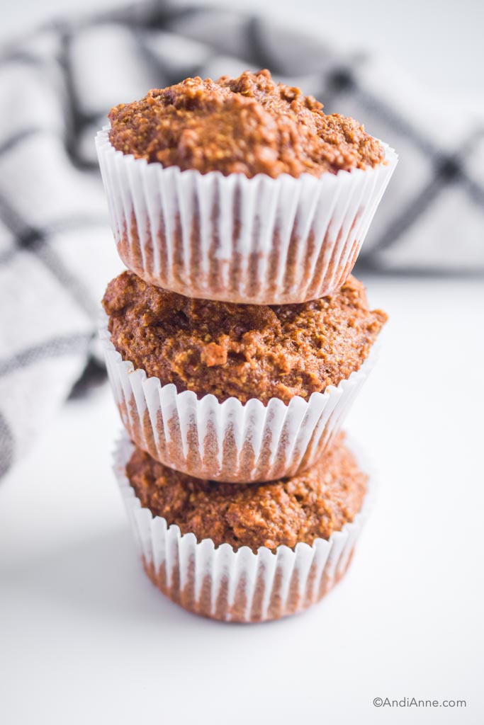 three flaxseed muffins stacked on top of eachother with white paper cupcake liners.