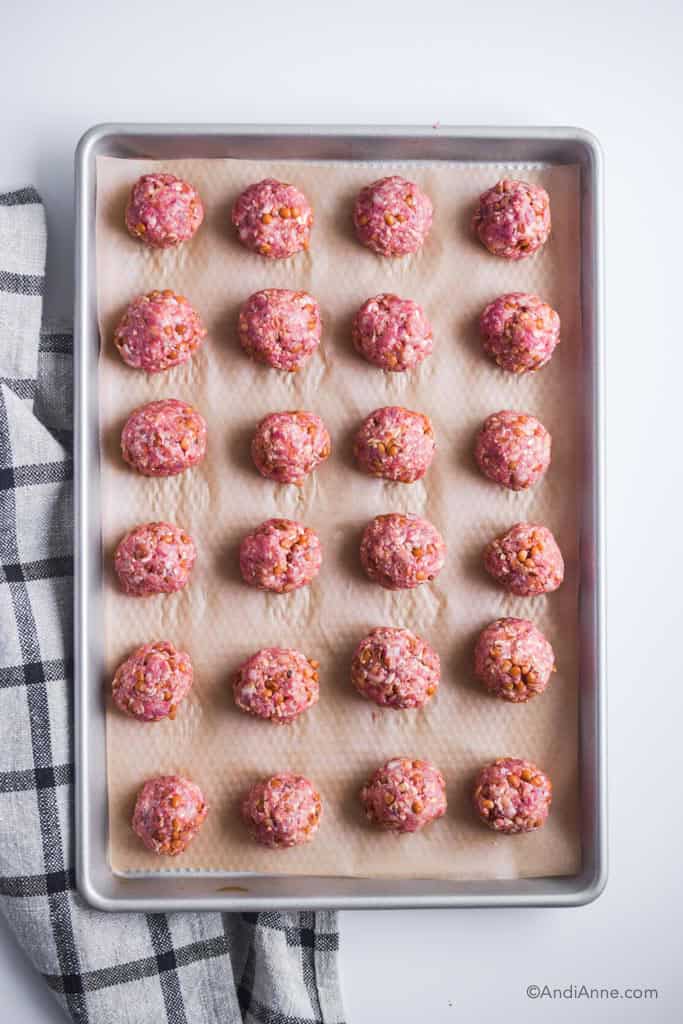 Baking sheet with raw meatballs on it. Kitchen towel beside it.