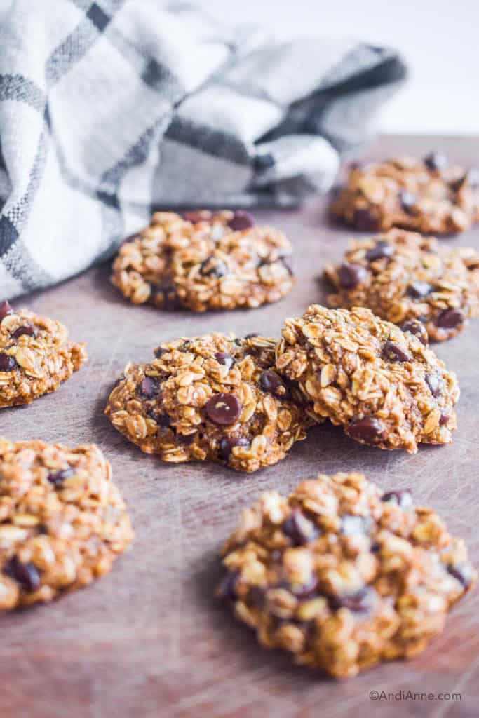 oatmeal chocolate chip cookies on a wood cutting board with kitchen towel behind it
