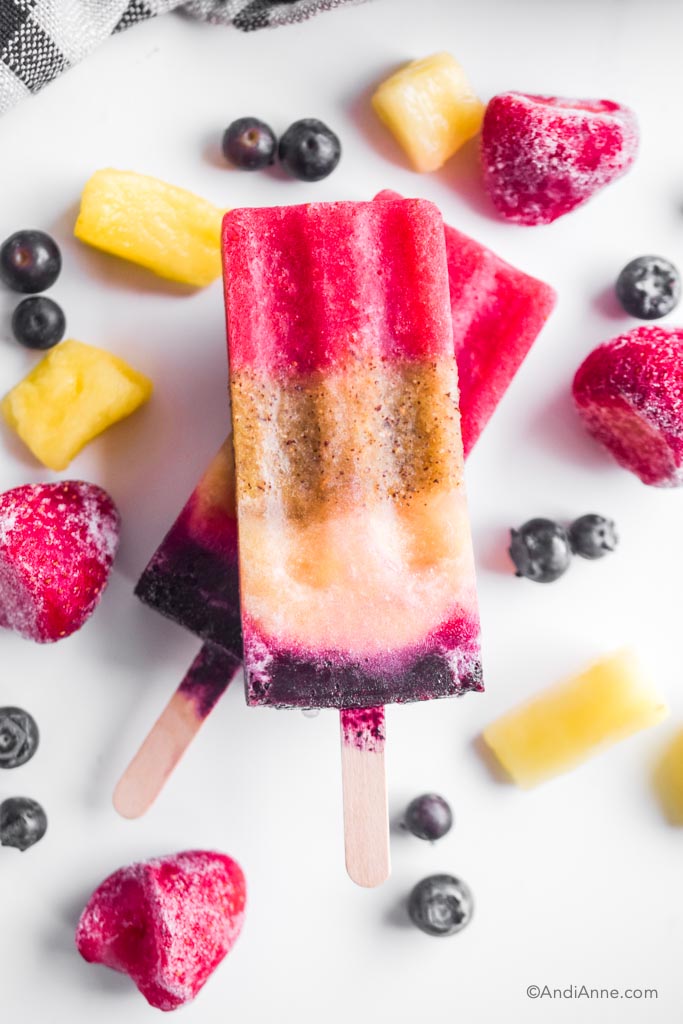 rainbow real fruit popsicles with frozen fruit around them