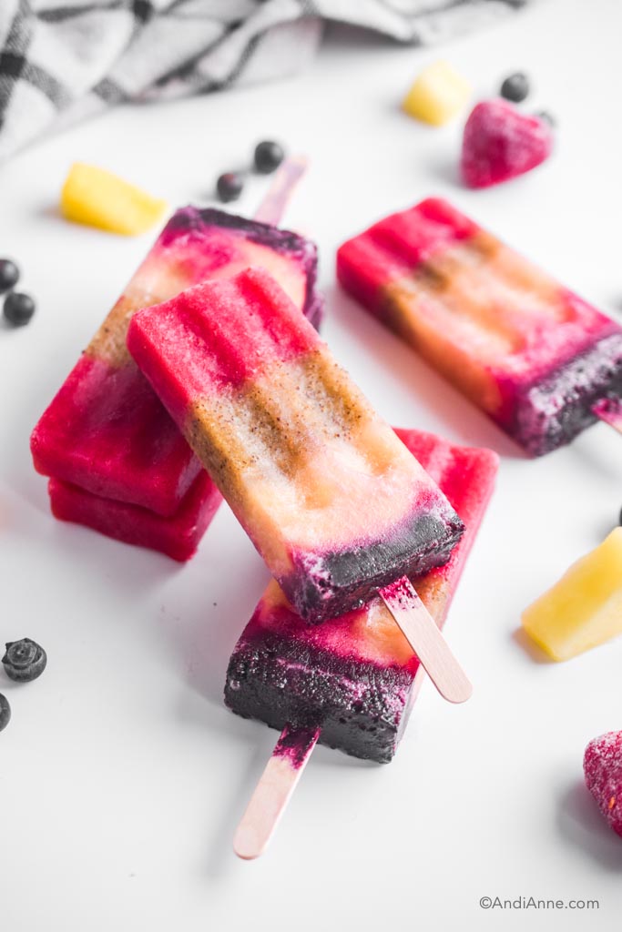 pile of fruit popsicles on a white table with frozen fruit surrounding them