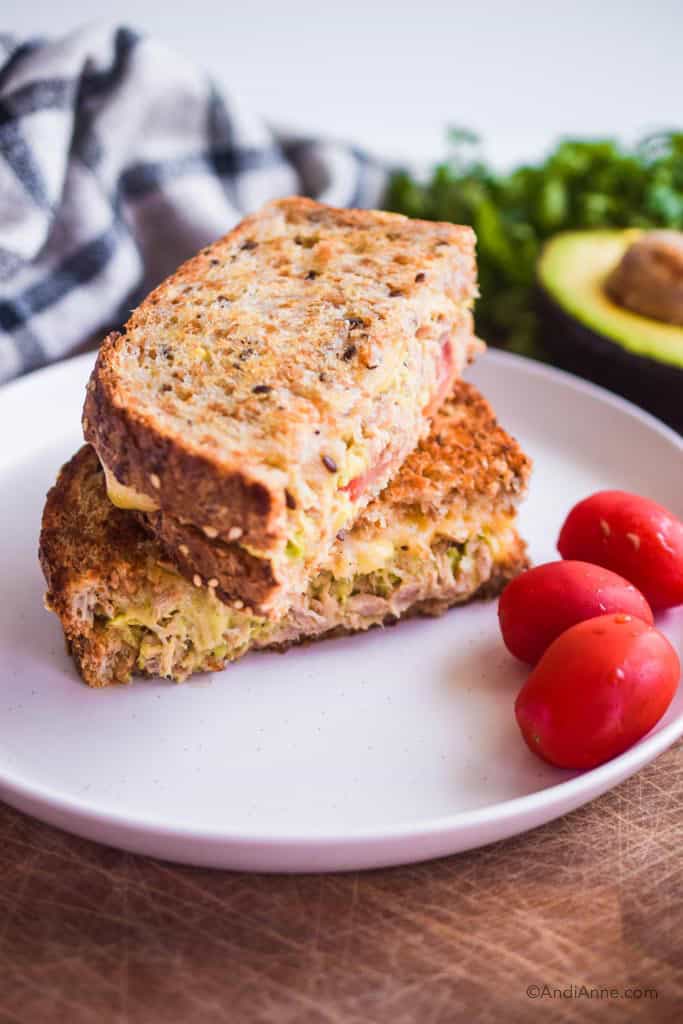 two slices of avocado tuna melt sandwich stacked on top of eachother. Three grape tomatoes beside it.