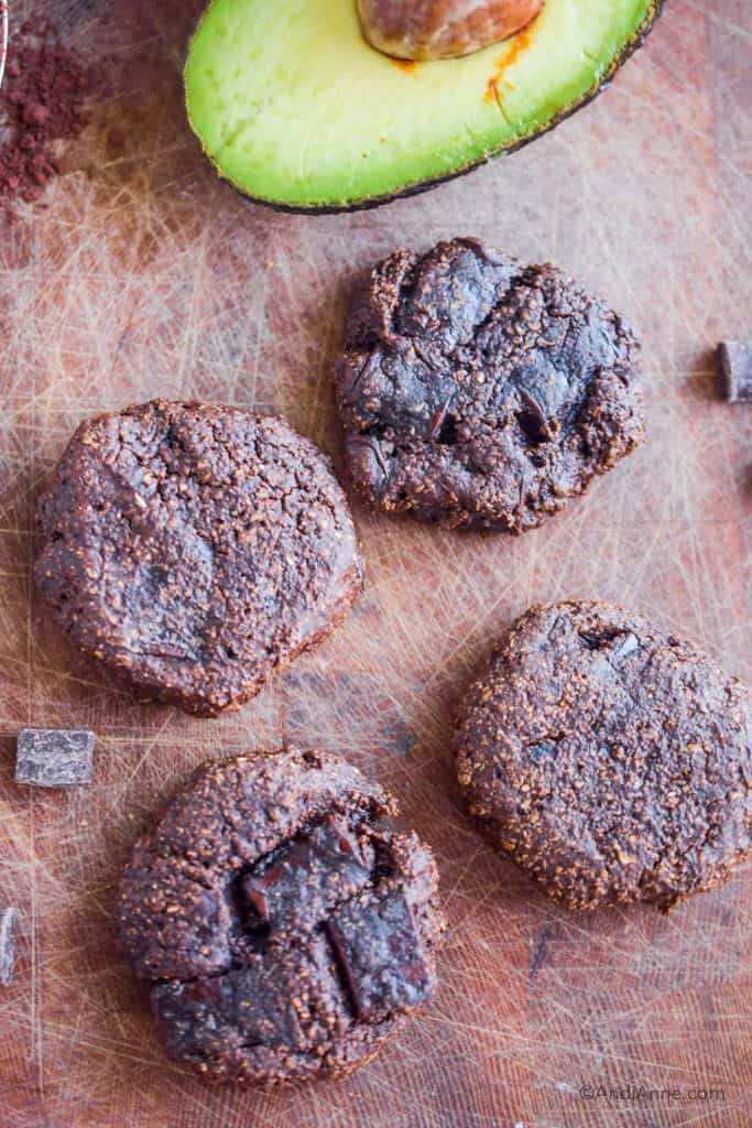 four chocolate avocado cookies on a cutting board with sliced avocado.