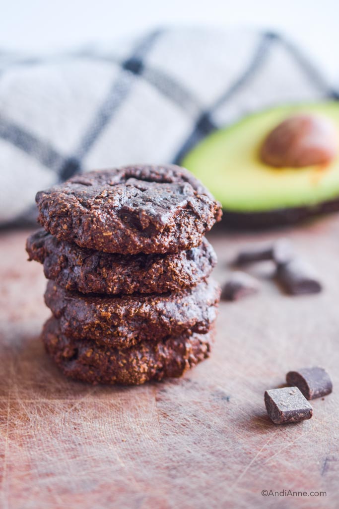 chocolate avocado cookies stacked on top of eachother. Sliced avocado in background.